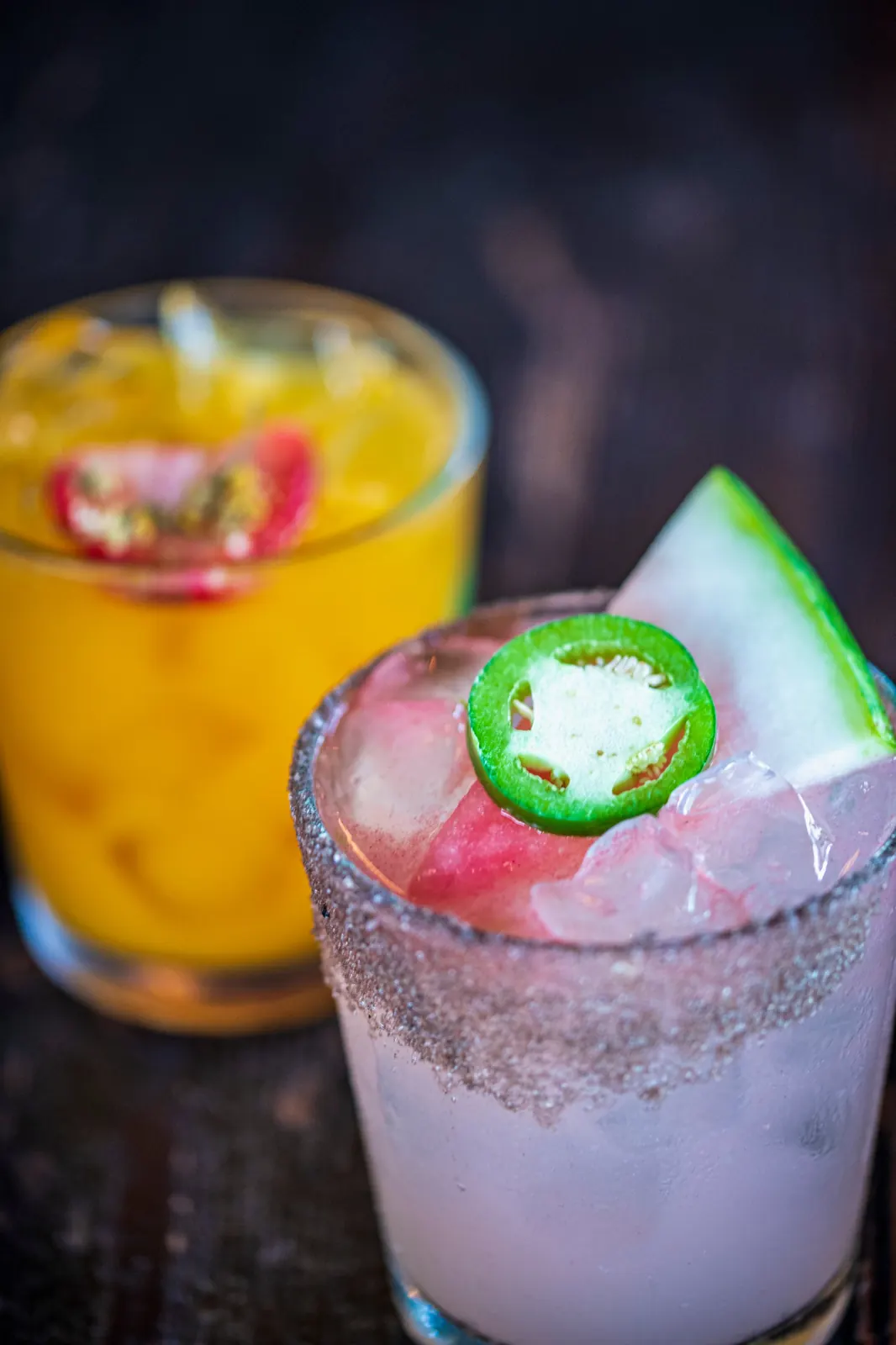 Watermelon jalapeño margarita with a jalapeño slice and an orange cocktail behind it