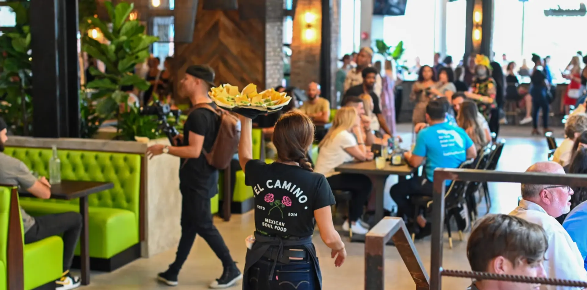 Server carrying a tray of chips and dips through a full dining room